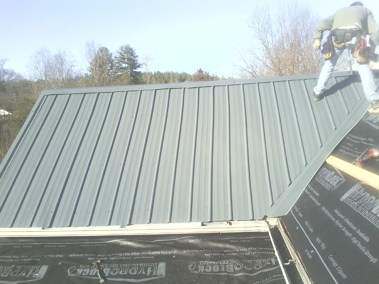 Crew installing dark green standing seam panels over synthetic underlayment in Norcross