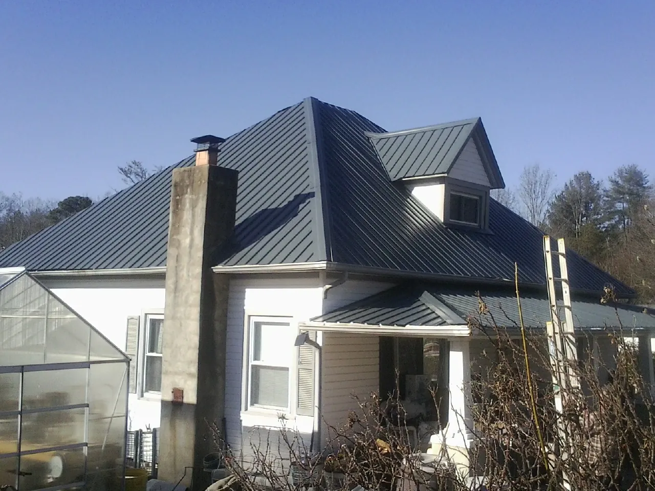 Dark blue standing seam metal roof on a white farmhouse with dormer — Slate & Tile Roof Repair by Roofing Brothers in Norcross