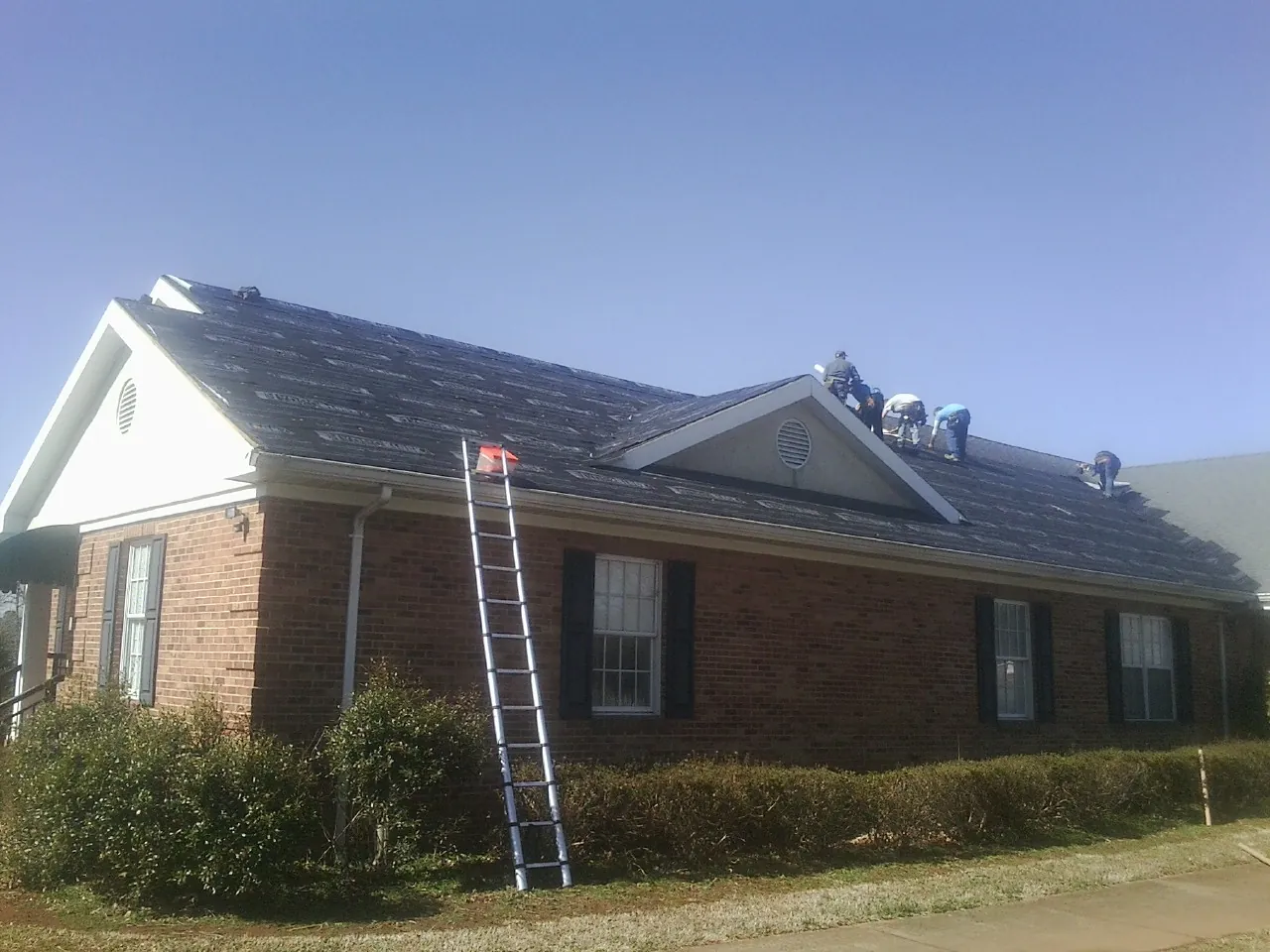 Crew tearing shingles off a brick ranch roof with a ladder set — Metal Roof Repair work by our crew in Norcross