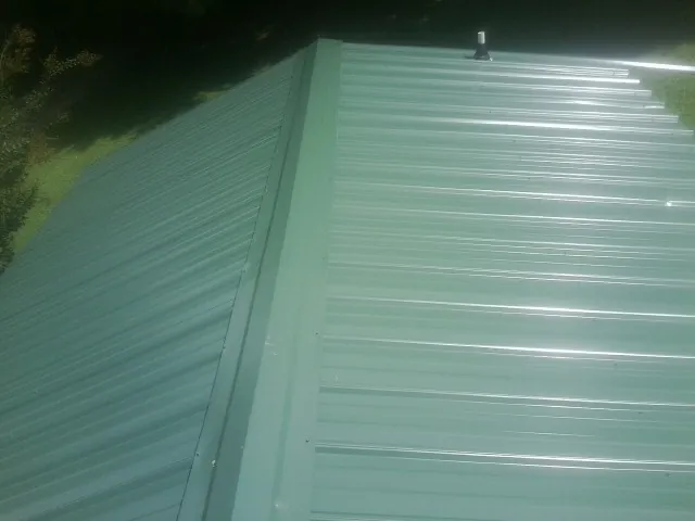 New green metal panels meeting at the ridge of a roof — Flat Roof Repair work by our crew in Norcross
