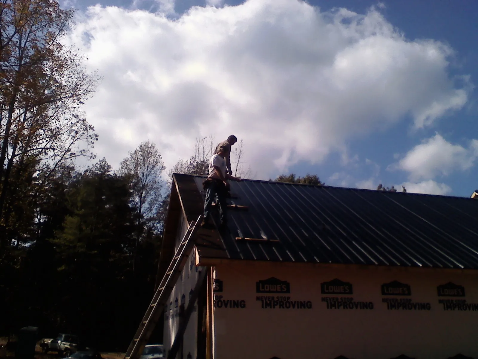 Roofer fastening dark metal panels high against a cloudy sky, from a Roof Inspection job in Norcross