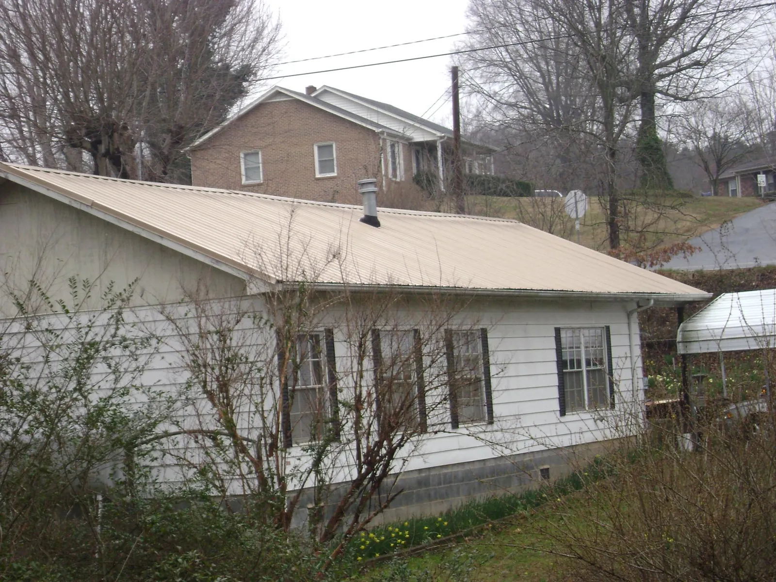 Tan metal roof on a white sided house set into a hillside — Commercial Roofing by Roofing Brothers in Norcross